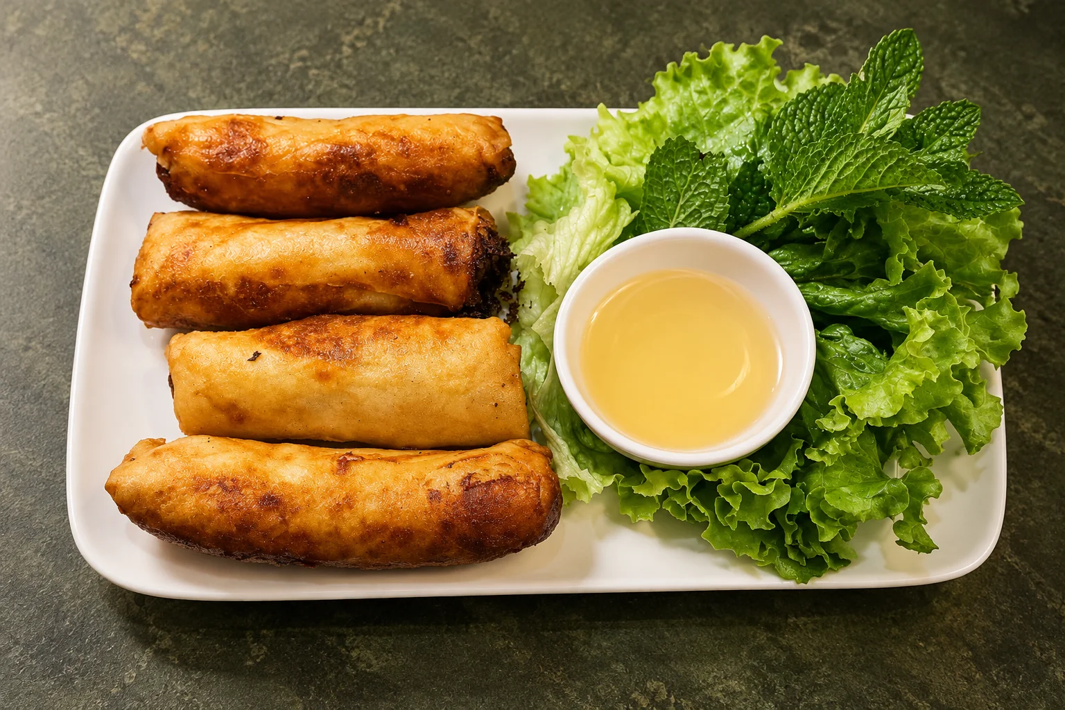N3. Vegetable spring rolls on a white rectangular plate, lettuce, mint and a sauce dish, on a dark green background